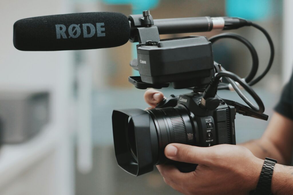 pexels-photo-2170450-2170450 Close-up of hands holding a professional video camera with a RØDE microphone attached.